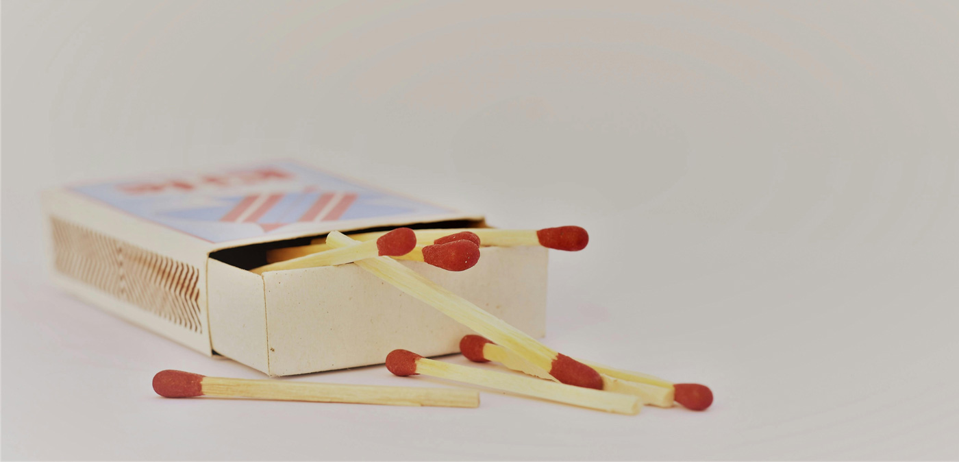 Open matchbox with red-tipped matches scattered on a white surface